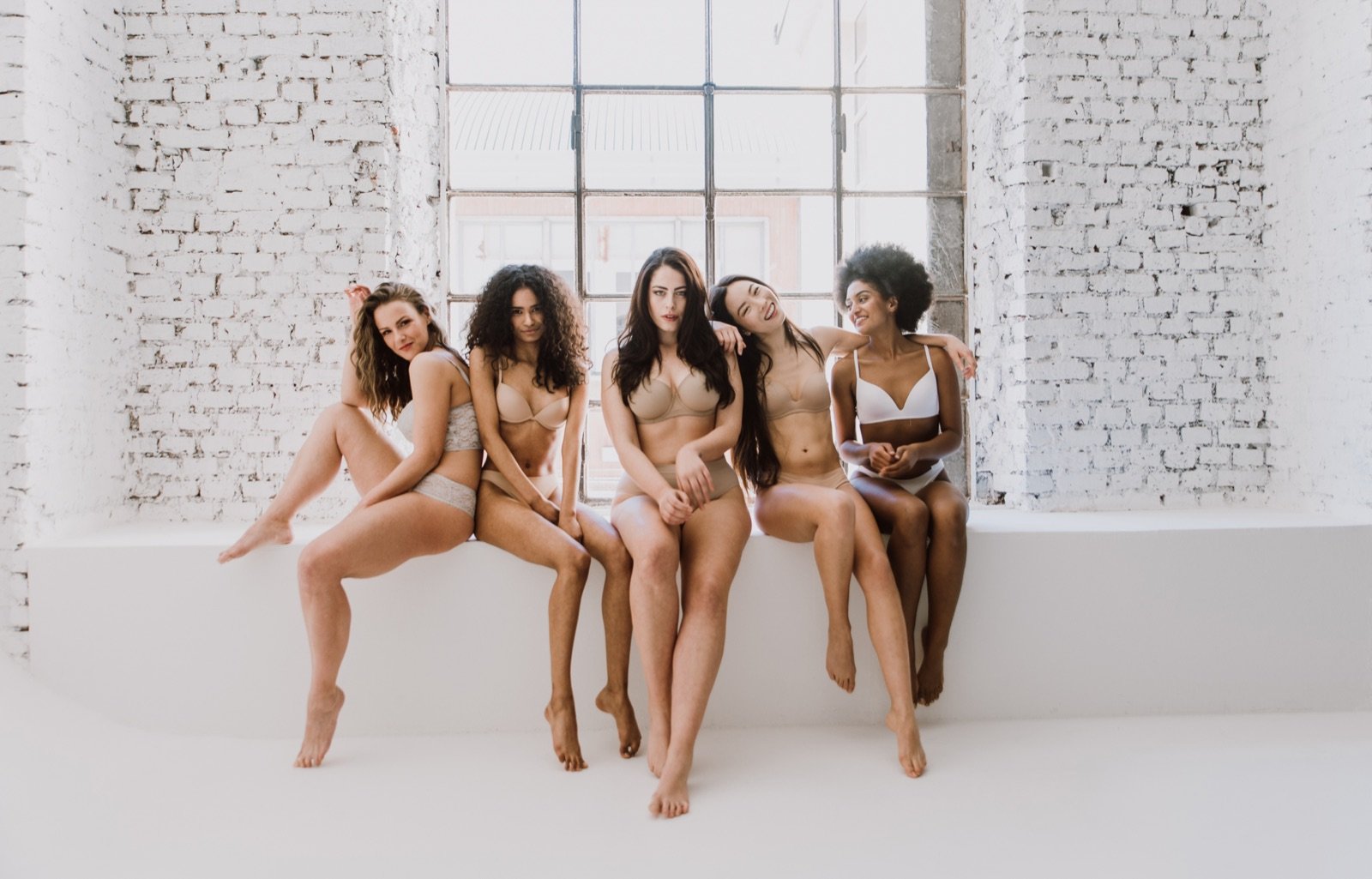 Five women of different bodies and backgrounds sitting together in a bright room